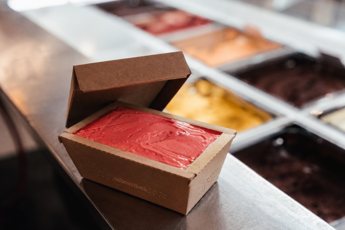 Eis zum Abholen: Kartonbox 500 ml mit rotem Fruchtsorbet vor der Eisvitrine